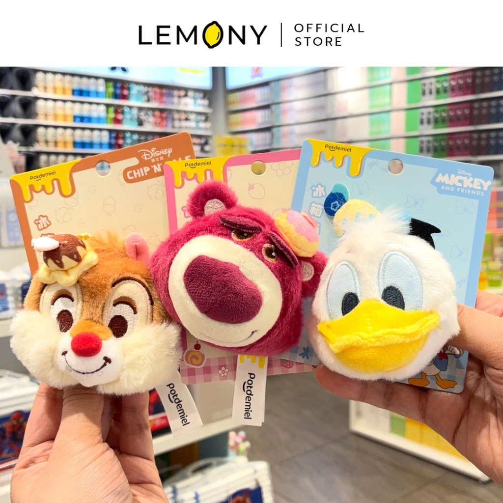 ภาพถ่ายสินค้าจริงของ LEMONY แม่เหล็กติดตู้เย็นตุ๊กตาขนนุ่ม ซีรีส์ Dessert ขณะมือถือโชว์ครบทั้ง 3 ลายบนแผ่นแพ็กเกจการ์ตูน ได้แก่ ลายเดลพร้อมพร็อพขนมหวาน, ลายล็อตโซ่ติดโดนัทจิ๋วบนหัว และลายโดนัลด์ดั๊กสวมหมวกกะลาสี แบคกราวด์ด้านหลังเห็นชั้นวางของในร้านค้า
