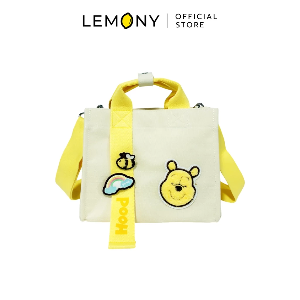 ภาพหลักฉากหลังขาวแสดงกระเป๋าถือและกระเป๋าสะพายพูห์ LEMONY Multi-Style Disney Winnie the Pooh Collection ลิขสิทธิ์แท้ ตัวกระเป๋าผลิตจากผ้าแคนวาสสีครีมทรงสี่เหลี่ยมคลาสสิก ด้านหน้าแต่งอาร์มปักหน้าหมีพูห์ขนฟูและสายริบบิ้นเหลืองปักคำว่า Pooh คู่ตัวการ์ตูนสายรุ้งกับผึ้ง มาพร้อมหูหิ้วและสายสะพายข้างสีเหลืองพาสเทลเข้าเซ็ต ด้านบนระบุโลโก้แบรนด์พรีเมียมชัดเจน