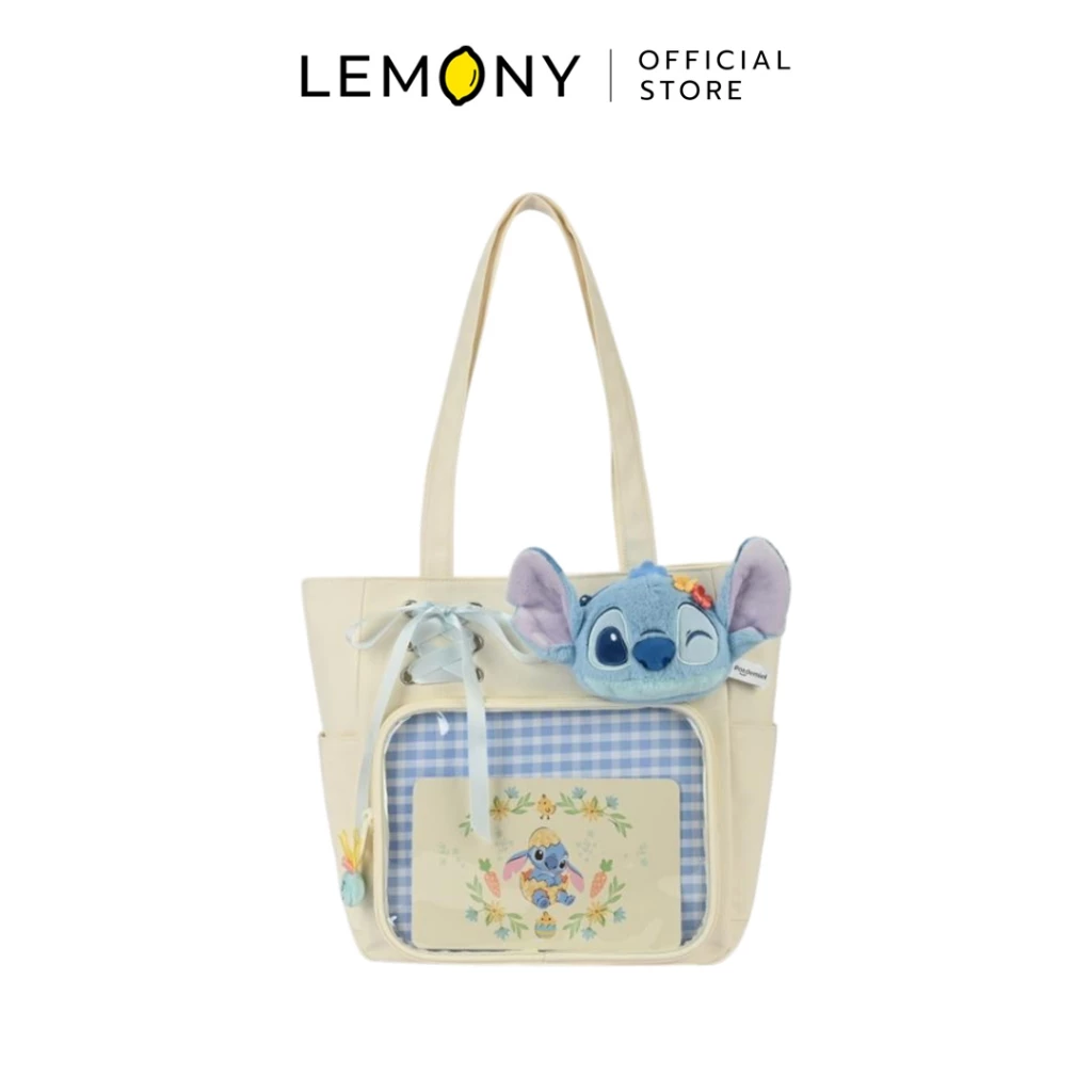 LEMONY กระเป๋าสะพายไหล่ดิสนีย์ ซีรีส์ Early Summer ลาย Stitch ตัวกระเป๋าผ้าสีครีมละมุน ช่องกระเป๋าด้านหน้าบุด้วยผ้าลายตารางสก็อตสีฟ้าพาสเทลสลับขาว ประดับด้วยหน้าตุ๊กตาสติทช์ขนนุ่มนิ่มกำลังกะพริบตาและติดดอกไม้สีส้ม พร้อมดีเทลเชือกร้อยโบว์สีฟ้าอ่อน