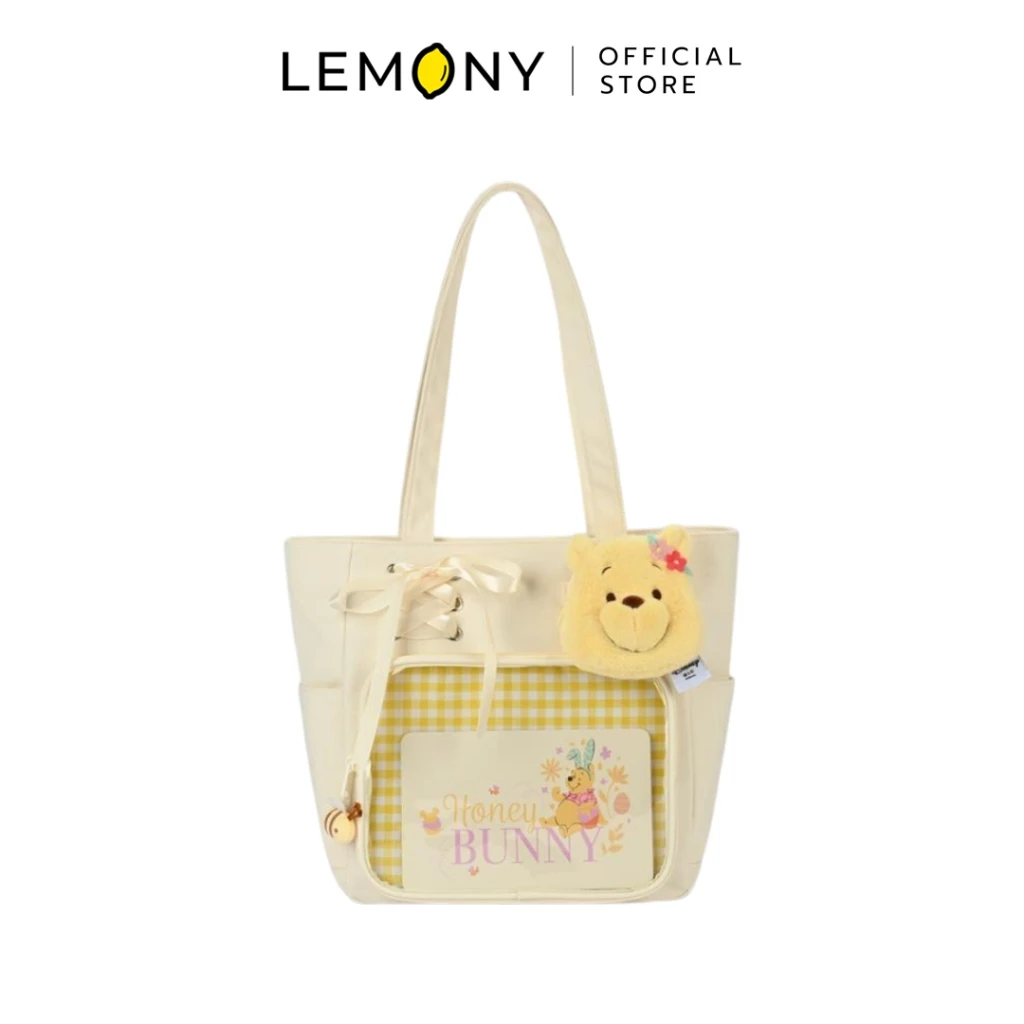 LEMONY กระเป๋าสะพายไหล่ดิสนีย์ ซีรีส์ Early Summer ลาย Winnie the Pooh ตัวกระเป๋าผ้าสีครีมละมุน ช่องกระเป๋าด้านหน้าบุด้วยผ้าลายตารางสก็อตสีเหลืองพาสเทลสลับขาว ประดับด้วยหน้าตุ๊กตาหมีพูห์ขนนุ่มนิ่มติดดอกไม้สีแดง และดีเทลเชือกร้อยโบว์สุดคิ้วท์ด้านข้างช่องกระเป๋า