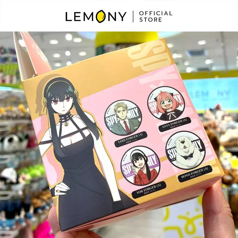 ภาพถ่ายสไตล์ไลฟ์สไตล์ เผยมุมมองมือที่กำลังถือโชว์กล่องกระดาษสุ่มสินค้า (Blind Box) อีกด้านหนึ่ง ซึ่งพิมพ์ลายกราฟิกตัวละครยอร์ ฟอร์เจอร์ (Yor Forger) ในชุดกระโปรงราตรีสีดำสายรัดคอสุดเท่ ข้าง ๆ แสดงรูปภาพตัวอย่างเข็มกลัดทรงกลมดีไซน์เวอร์ชัน A จำนวน 4 ลาย ได้แก่ ลอยด์, อาเนีย, ยอร์ และสุนัขบอนด์ โครงสร้างกล่องพับปิดสนิทเรียบร้อย ด้านบนสุดระบุโลโก้แบรนด์ LEMONY Official Store