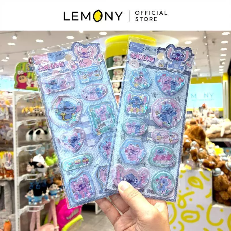 ภาพถ่ายสไตล์ไลฟ์สไตล์ เผยมุมมองมือที่กำลังถือชูแผ่นการ์ดสติกเกอร์น้ำสามมิติกลิตเตอร์โชว์พร้อมกันทั้ง 2 ลายหลัก ฝั่งซ้ายคือลายแองเจิล (Angel) สีชมพูพาสเทล ฝั่งขวาคือลายสติทช์ (Stitch) สีฟ้าสดใส ฉากหลังเป็นบรรยากาศชั้นวางสินค้าและของเล่นในร้านค้า ด้านบนสุดระบุโลโก้แบรนด์ LEMONY Official Store