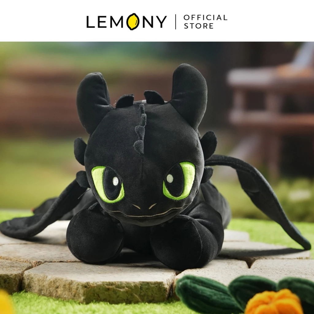 ภาพถ่ายชิ้นงานตุ๊กตาเขี้ยวกุดจากมุมหน้าตรงระดับสายตา โชว์ใบหน้ามังกรราตรีเพลิงนิลสีดำกลมมน ดวงตาสีเขียวขอบดำคูโตปักเข็มประณีต ท่วงท่านอนหมอบราบและขยายกางปีกออกสองข้างเล็กน้อยอย่างบาลานซ์สวยงาม ตั้งวางบนพื้นหินในสวน ด้านบนสุดระบุโลโก้ LEMONY Official Store
