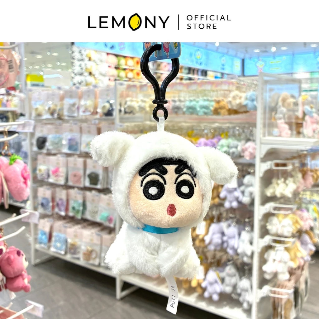 ภาพถ่ายสินค้าจริงในร้านค้า เผยพวงกุญแจตุ๊กตาชินจังคอสเพลย์ชุดสุนัขชิโร่สีขาวงาช้างขนปุยหนานุ่มนิ่ม แขวนโชว์หน้าตรงสะดุดสายตาด้วยตัวล็อกพลาสติกสีดำสนิท มีป้ายริบบิ้นสีขาวสกรีนคำว่า Pull it ห้อยอยู่ด้านล่าง ฉากหลังเป็นชั้นวางของเล่นและตุ๊กตาภายในร้าน ด้านบนระบุตราสัญลักษณ์ร้านค้า LEMONY Official Store